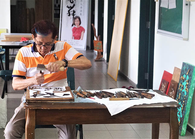 A practitioner skilfully chisels away the wood on a new signboard.